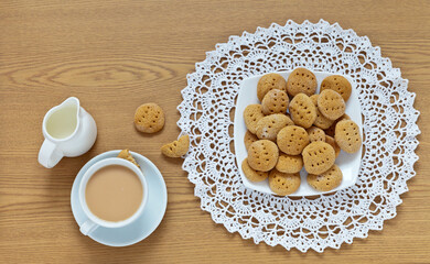 Freshly baked honey cookies on a lace napkin and a cup of tea with milk on a wooden table. Delicious healthy homemade cakes for breakfast for the holiday. Flat lay, close-up, top view