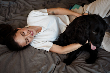 Smiling young brunette woman petting her dog at home