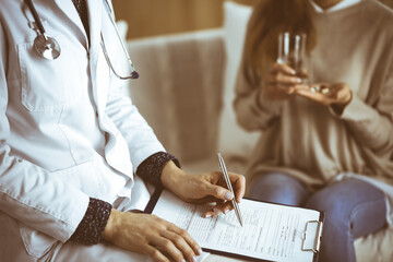 Unknown woman-doctor and patient discussing current health examination while sitting indoors. Stay...