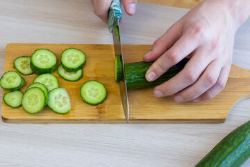 A young man carefully cuts a cucumber with a knife on a cutting board.