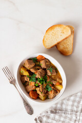 Goulash, beef stew with vegetables and thyme in a white plate with onion and greens.