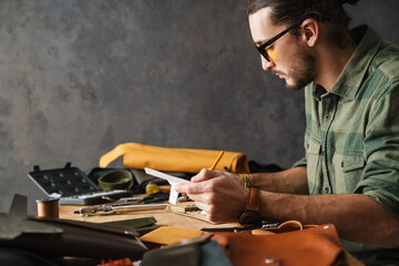 Bearded focused craftsman writing down notes while sitting at table