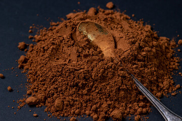 Cocoa powder on a black background. The spoon lies in cocoa powder on a dark background.