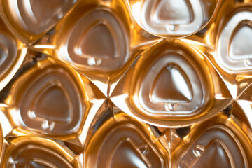 A box of round candies in golden foil on a black background. Wrapped chocolates. Round cake. Sweet food. Sweet gift. Golden color. Food photo. Product. Delicacy. Background image.