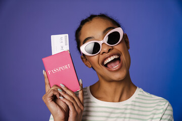 Excited black woman in sunglasses holding passport with ticket
