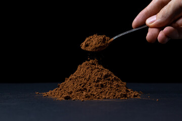 Cocoa powder on a black background. Spoon of cocoa powder on a dark background.
