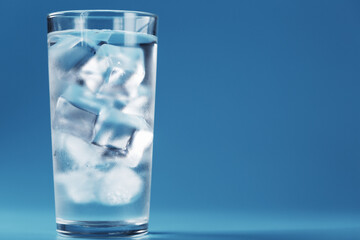 Ice cubes in a glass with crystal clear water on a blue background.
