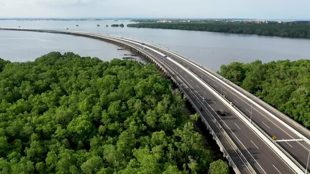 Bike and car advance on the Mandara Toll Road at the Gulf of Benoa in Bali Indonesia,  Aerial follow forward shot