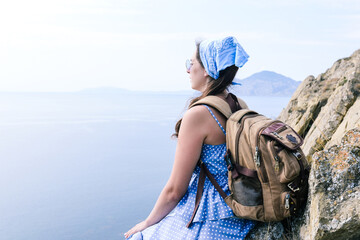 The traveler sits on top of a cliff and admires the beautiful scenery. Girl with a backpack near...