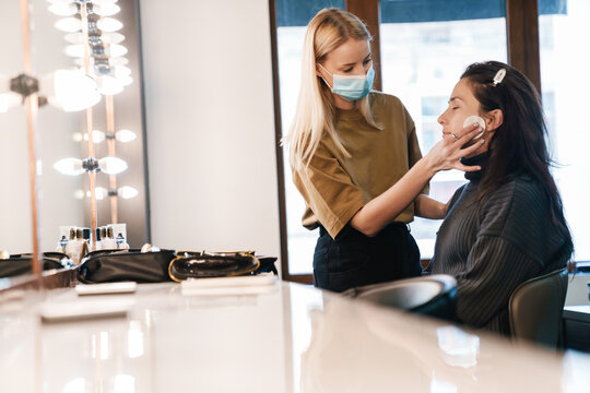 Young blonde woman in face mask working with client in beauty salon