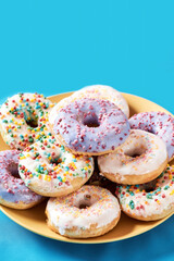 Light and fluffy dessert. Close up shot of different colourful round glazed donuts with sprinkles on yellow plate over blue background