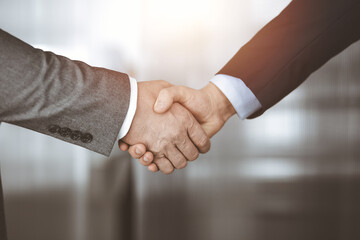 Business people standing and shaking hands in sunny office, close-up. Handshake and marketing