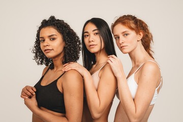 Photo of optimistic young women, multiracial friends wear underwear, hug each other and show their love. Concept natural beauty and girl power