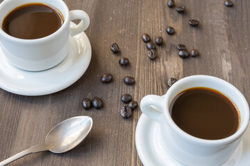 Aerial view of two white cups with coffee and spoon, on wooden table with coffee beans, selective focus, horizontal