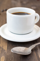Close-up of metal spoon and white coffee cup with saucer on dark wooden table, selective focus, vertical, with copy space