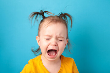 Upset little baby girl crying on blue background. Top view