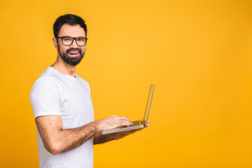 Confident business expert. Confident young handsome bearded man in casual holding laptop and smiling while standing over isolated yellow background.
