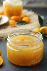 Delicious kumquat jam in glass jar on grey table
