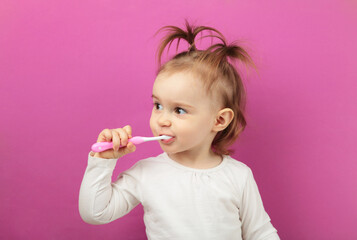 Cute baby girl brushing teeth on pink background.