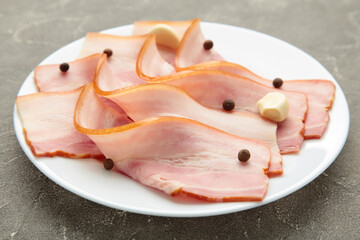 Fresh raw slices bacon on plate on grey background. Vertical foto