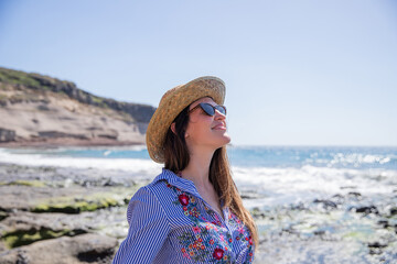 Girl at the beach relaxes and enjoys the holidays, she wears sunglasses and a summer hat