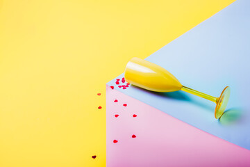 Red Heart-shaped confetti falling from yellow wine glass lying on the pink and blue podium on the...