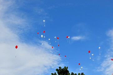 Hoch hinauffliegende rote und weiße Herz-Luftballons mit anhängender Karte vor blauem Himmel