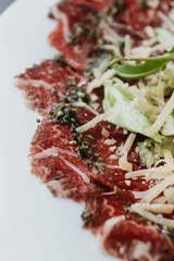 Classic beef carpaccio with cheese and arugula on a ceramic plate, served with lemon. Makro.