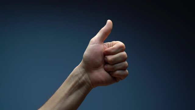 Close up of man hand pointing to the left side showing thumb up sign isolated on a blue studio background with copy space for place a text, message for advertisement, and promotional