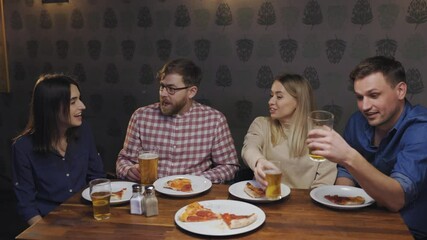 Happy friends sit at the table in pub eat pizza watch tv and talk with each other.