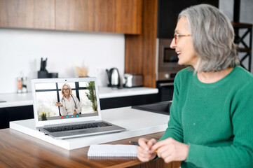 Fototapeta na wymiar Senior female patient using computer app for video communication with a doctor. Elderly woman with a laptop talking with a therapist online. Telemedicine concept