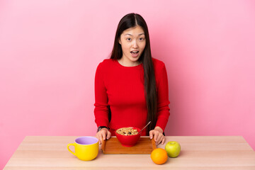 Young Chinese girl  having breakfast in a table with surprise facial expression