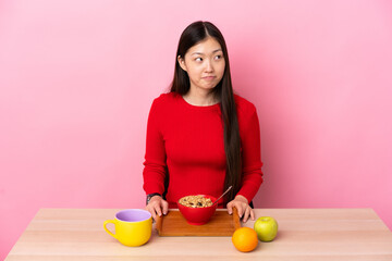 Young Chinese girl  having breakfast in a table having doubts while looking up
