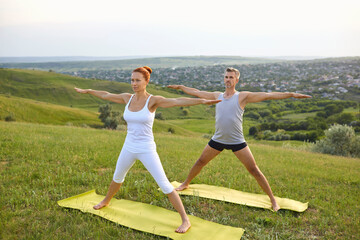 Middle aged couple doing Five Pointed Star asana while practicing yoga together on grassy hill