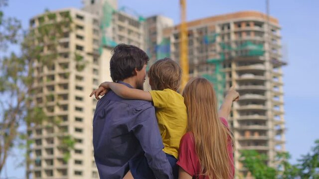 A family father, mother, and son look at a tall building that is under construction. They are discussing where they should buy an apartment