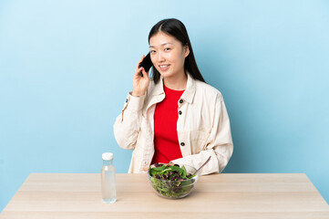 Young Chinese girl eating a salad keeping a conversation with the mobile phone with someone