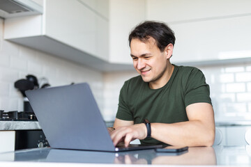 Handsome man using a laptop in the kitchen. Working from home in quarantine lockdown. Social distancing Self Isolation