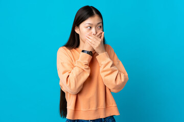 Young Chinese girl over isolated blue background covering mouth and looking to the side