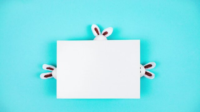 4k Three white eggs and three Easter bunnies appear and hide behind a sheet of white paper. Happy Easter Day Concept. Light blue background. Template for text. Stop motion animation. Copy space.
