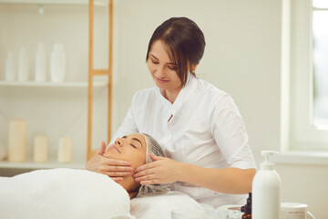 Obraz na płótnie Canvas Smiling woman dermatologist making manual relaxing facial massage for woman