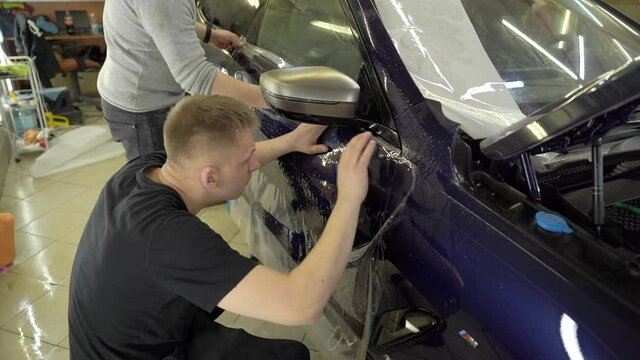 Two guys gluing a protective film on the car door