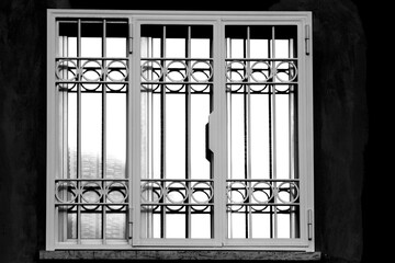 Closed window with anodized steel protective grating, light reflections on the glass, black and white photo