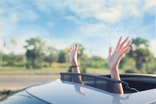 woman putting his hands out of the car sunroof top, driving down a country road