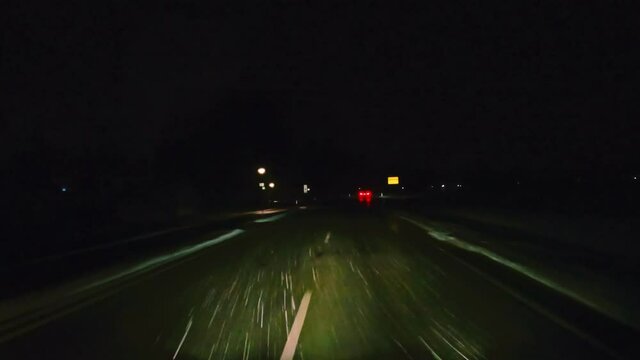 Driving by night over a wet, snowy street, snow is falling enlighted by the headlights of a car. Drivers view at bad slippery conditions.