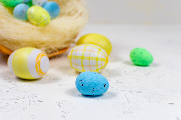 Multi-colored Easter eggs painted in pastel colors on a white table against the background of a basket of Easter eggs. Selective focus. Place for an inscription. Close-up.