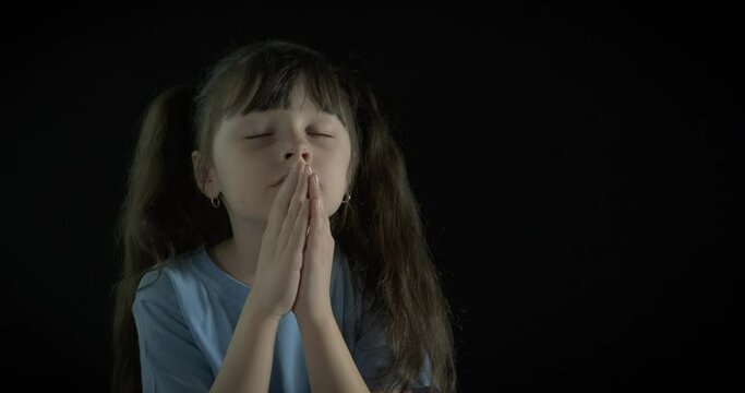 A child in prayer. Cute little girl prays on a black background.