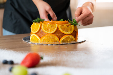 Young pastry chef cooking an orange cake with sliced oranges