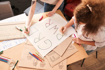 Girls drawing handmade poster about feminism at the table with each other