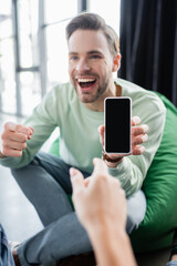amazed businessman showing mobile phone with blank screen to coworker on blurred foreground
