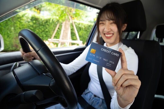 Happy young Asian woman driver holding payment card, member card, credit card and sitting in car